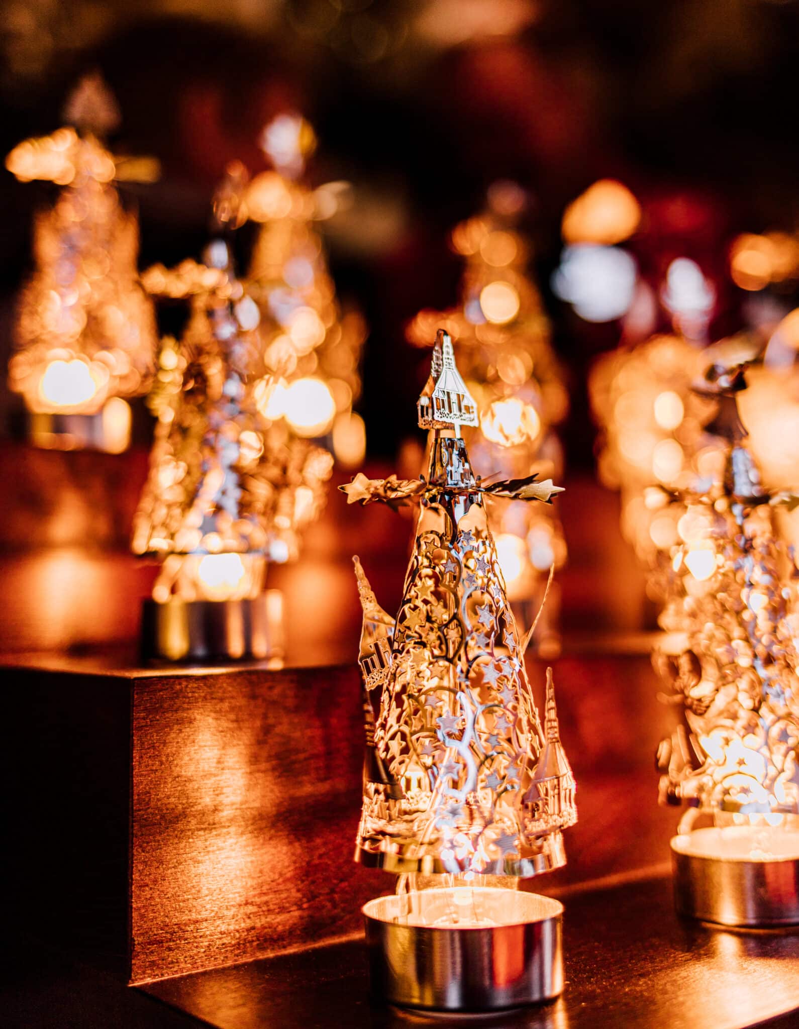 Nahaufnahme, stimmungsvoll leuchtende Detailansicht von Teelichtern mit weihnachtlichen Metall-Ornamenten an einem Verkaufsstand auf dem Dachauer Christkindlmarkt.