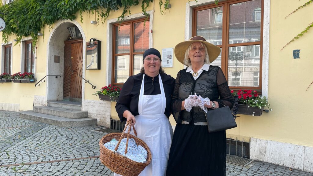 Foto von Dachauer Gästeführerinnen in Kostümen bäuerlich und feine Dame, Kostümführung "gschnipfige Henne", vor dem Eingang des ehemaligen Zieglerbräu.
