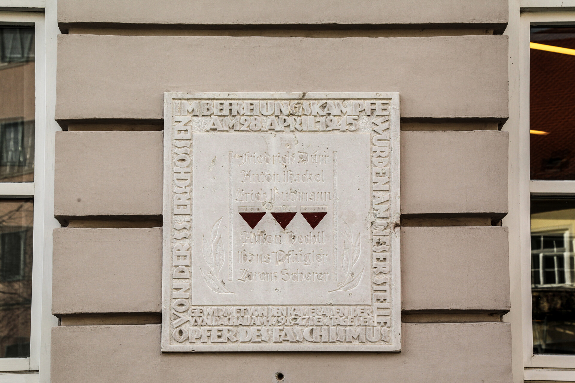 Blick auf quadratische Gedenkstafel für die Opfer des Dachauer Aufstandes im April 1945. Die Tafel ist an der Fassade der Gemäldegalerie Dachau befestigt. Die Inschrift darauf lautet: "Im Befreiungskampfe am 28. April 1945 wurden an dieser Stelle Opfer des Faschismus von der SS erschossen. Gewidmet den Kameraden vom V.V.N. Dachau am 14.9.1947, Friedrich Dürr, Anton Hackel, Erisch Hubmann, Anton Hechtl, Hans Pflügler, Lorenz Scherer.