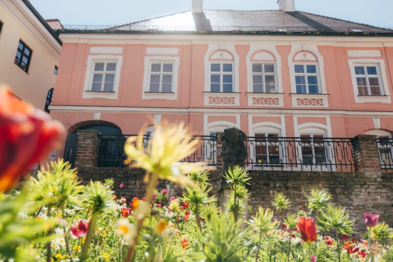Außenansicht des Bezirksmuseums über ein Blumenbeet hinweg auf die rosafarbene Fassade.