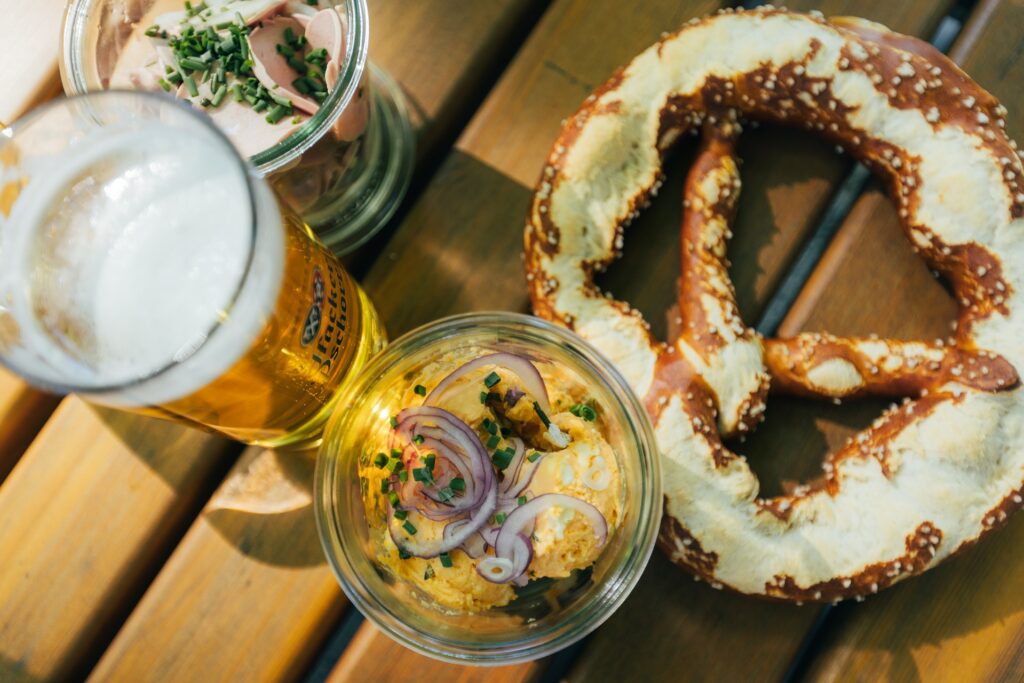 Nahaufnahme von Biergarten Brotzeit von oben mit einem Glas Bier, Obazda, Wurstsalat und Breze.