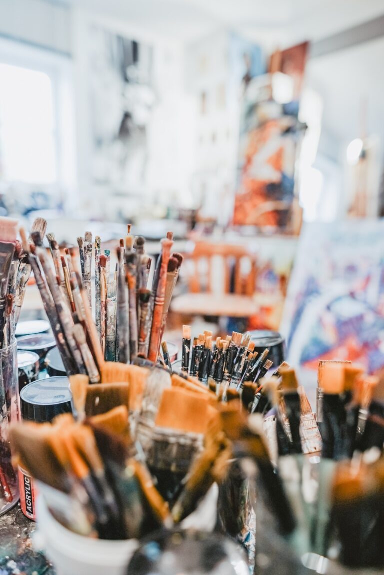 Fotografie in einem Atelier in Dachau, im Vordergrund viele Pinsel und Farben und im Hintergrund unscharf, Bilder des Künstlers Stupka.